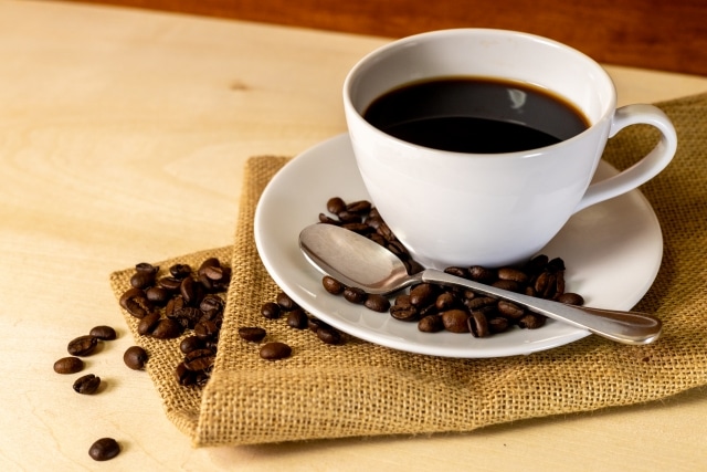 カップに入ったコーヒーとちりばめられたコーヒー豆 